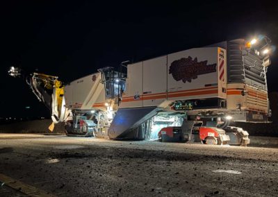 Nighttime road work with an illuminated asphalt milling machine on a construction site.
