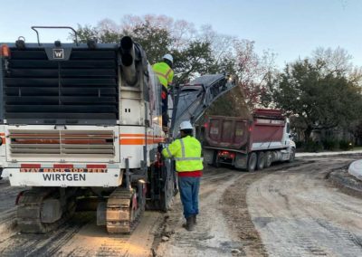 Milling machine and workers removing old pavement in a residential area.