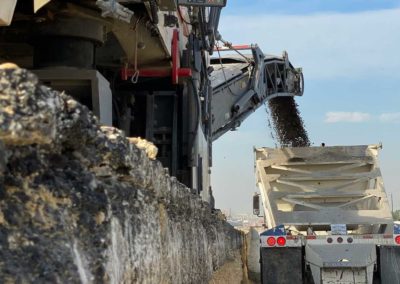 Tracked milling machine loading reclaimed asphalt pavement into a truck for removal.