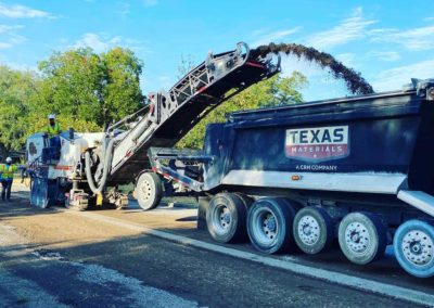 Road milling machine transferring milled asphalt into a dump truck under sunny skies.
