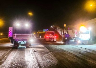 Milling operations on a highway at night with heavy machinery.