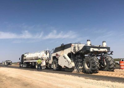 Workers operating heavy machinery for soil stabilization on a dirt road for a new highway project.