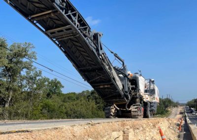 Low-angle view of a milling machine operating on a road construction site with an elevated conveyor.