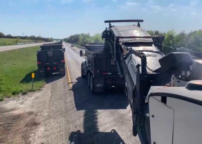 Road milling machine in action with trucks positioned to collect the milled asphalt.